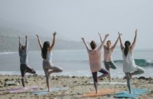 a group of people in fitness clothes doing standing yoga poses on the sand in front of the sea